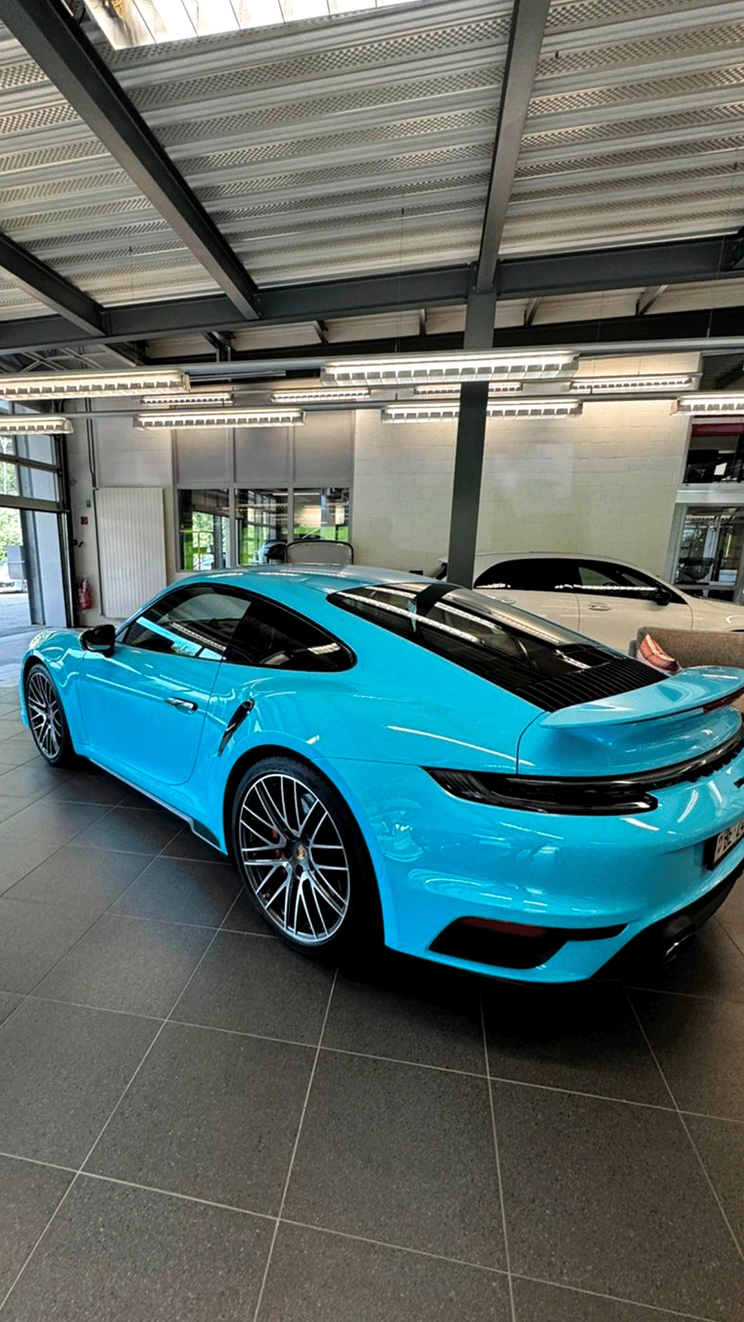 Porsche 911 turquoise avec covering brillant exposée dans un showroom à Genève